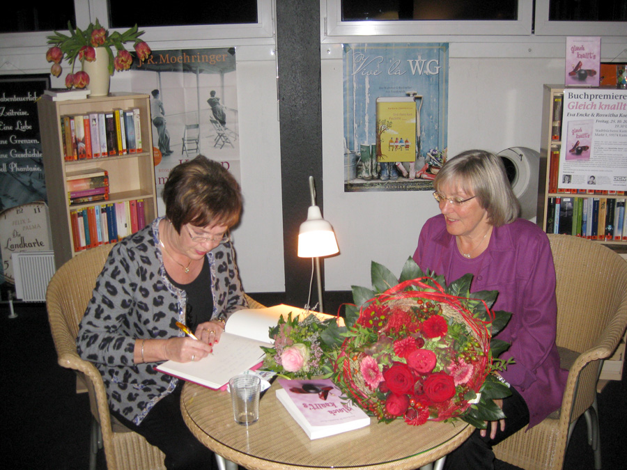 Roswitha Koert und Eva Encke sitzen an einem Tisch und signieren Bücher