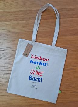 Preview: Draufsicht einer beigen Bio-Baumwolltasche auf einem Holzuntergrund, bedruckt mit dem bunten Spruch 