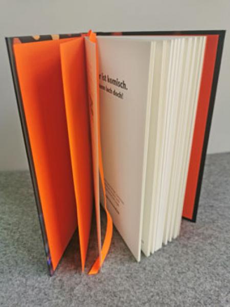 Blick in das offene Buch mit orangefarbenem Vorsatzpapier und Lesebandchen. Blick in das offene Buch mit orangefarbenem Vorsatzpapier und Lesebandchen.